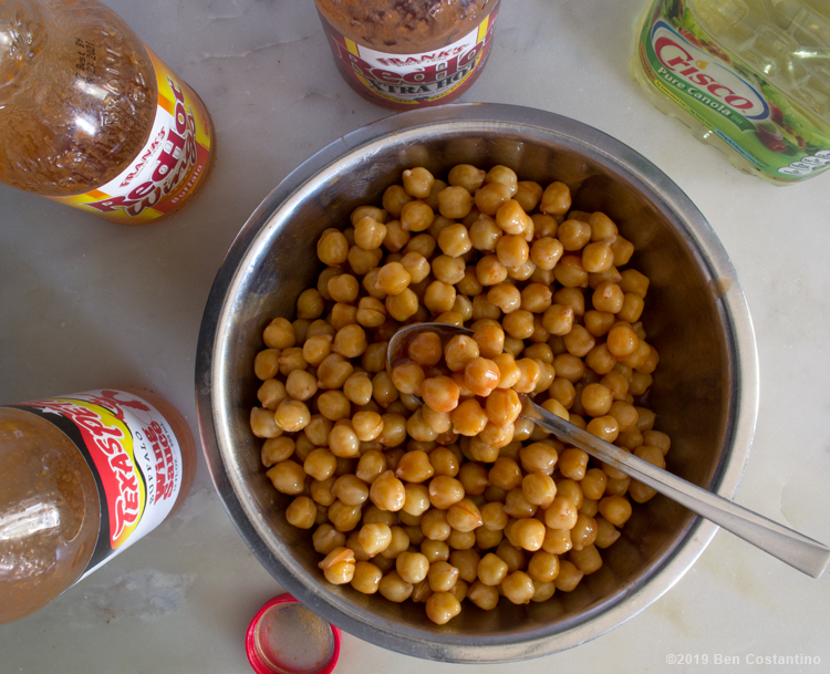 chickpeas being mixed in a bowl with canola oil and Texas Pete Hot Sauce and Franks Red Hot Sauce